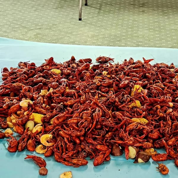 A large pile of red boiled crawfish, corn, and potatoes on a blue tablecloth.