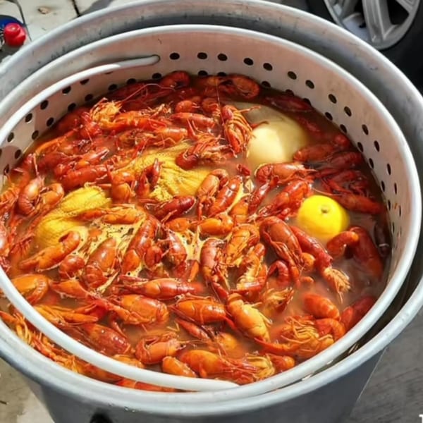 A large pot filled with bright red Cajun crawfish, corn, and lemons in a flavorful broth.