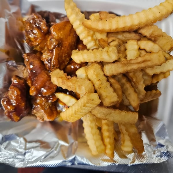 Dat Bayou Spot's Cajun wings coated in sauce next to a pile of crinkle-cut fries.
